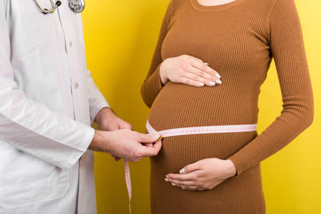 happy beautiful pregnant young woman touching her bare tummy while a doctor is measuring it.の写真素材