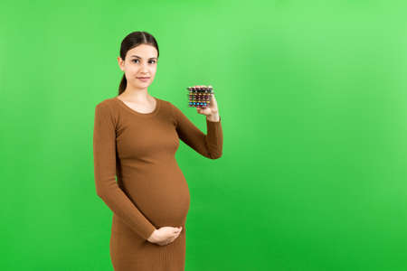 pregnant woman holding a pile of blisters of pills at colorful background with copy space. Vitamins during pregnancy concept.の写真素材