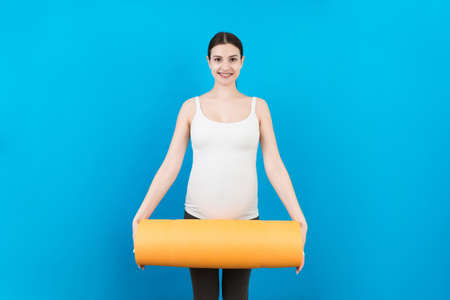 Pregnant Girl Holding Yoga Mat Standing Over Colored Background. Studio Shot, Free Space For Design.の写真素材