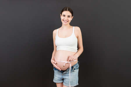 pregnant woman using tape measure to check baby development and the growth of belly. Inch...