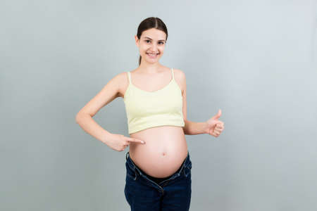 Young beautiful teenager girl pregnant expecting baby over isolated colored background smiling showing big belly.の写真素材