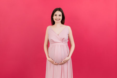 Happy pregnant woman touching her abdomen at Colored background. Future mother is wearing white underwear. Expecting of a baby. Copy space.の写真素材