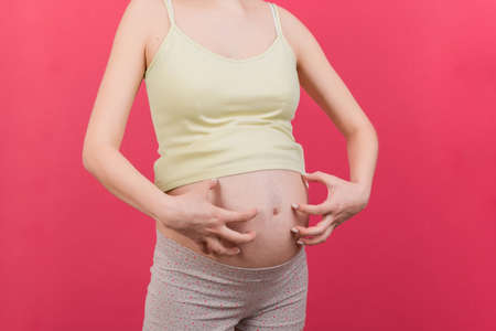 Pregnant woman scratching her belly on colored background.の写真素材