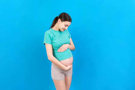 Happy pregnant woman touching her abdomen at Colored background. Future mother. Expecting of a baby. Copy space.の写真素材