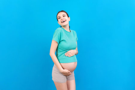 Happy pregnant woman touching her abdomen at Colored background. Future mother is wearing white underwear. Expecting of a baby. Copy space.の写真素材