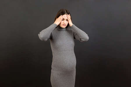 Beautiful young pregnant woman feeling head ache on colored background isolated. Stressed pregnant woman or mother problems.の写真素材