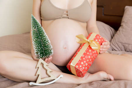 Happy pregnant woman holding Christmas gift box in her hands. New year concept.の写真素材