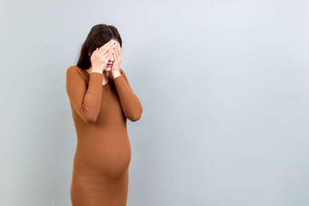 Beautiful young pregnant woman feeling head ache on colored background isolated. Stressed pregnant woman or mother problems.の写真素材