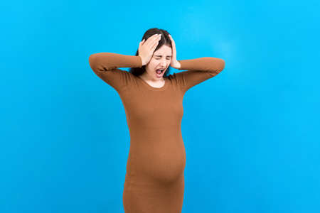 Beautiful young pregnant woman feeling head ache on colored background isolated. Stressed pregnant woman or mother problems.の写真素材