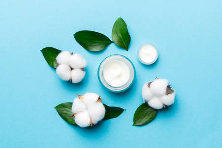 Organic cosmetic products with cotton flower and green leaves on wooden background. Flat lay.