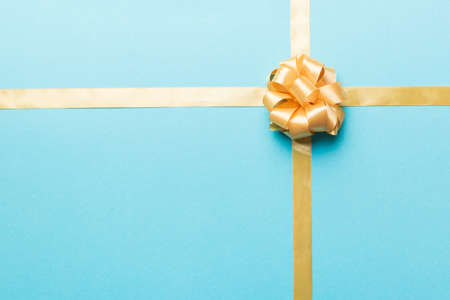 Top view of gold ribbon rolled and yellowbow isolated on colored background. Flat lay with copy space.の写真素材