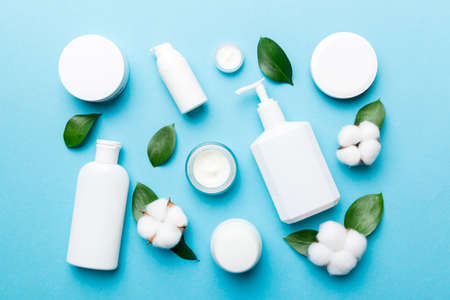 Organic cosmetic products with cotton flower and green leaves on wooden background. Flat lay.