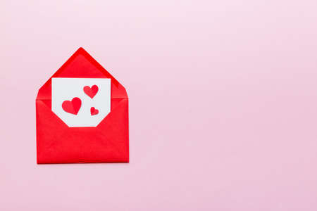 Red paper envelope with empty white card and heart on colored background. top view valentines day concept.の写真素材