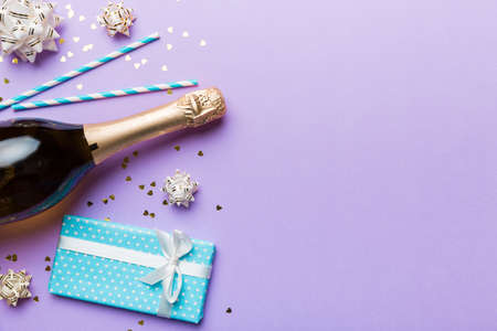 Bottle of champagne with colored glitter, confetti and gift box space for text on colorfull background, top view. Hilarious, christmas and birthday celebration.の写真素材