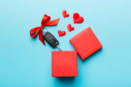 Black car key in a present box with a ribbon and red heart on colored background. Valentine day composition Top view.の写真素材