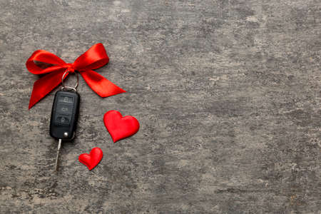 Car key with a red bow and a heart on Colored table. Giving present or gift for valentine day or christmas, Top view with copy space.の写真素材