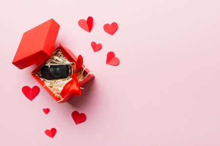 Black car key in a present box with a ribbon and red heart on colored background. Valentine day composition Top view.の写真素材