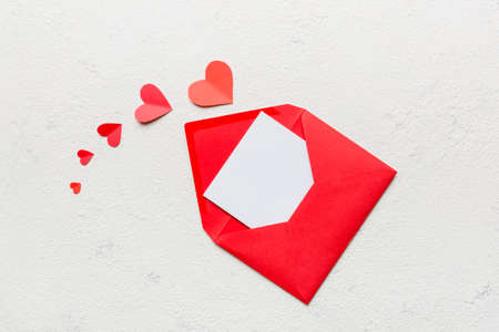 Red paper envelope with empty white card and heart on colored background. top view valentines day...