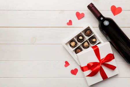Bottle of red wine on colored background for Valentine Day with gift and chocolate. Heart shaped with gift box of chocolates top view with copy space.の写真素材