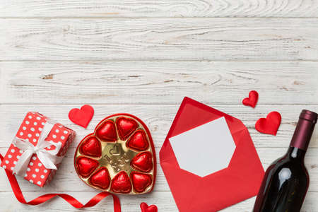 Bottle of red wine on colored background for Valentine Day with gift box, envelope and chocolate. Heart shaped with gift box of chocolates top view with copy space.の写真素材