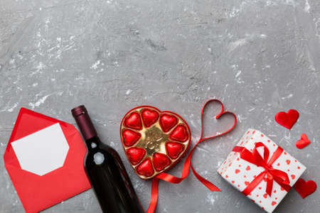 Bottle of red wine on colored background for Valentine Day with gift box, envelope and chocolate. Heart shaped with gift box of chocolates top view with copy space.の写真素材