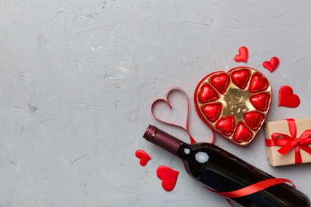 Bottle of red wine on colored background for Valentine Day with gift and chocolate. Heart shaped with gift box of chocolates top view with copy space.の写真素材