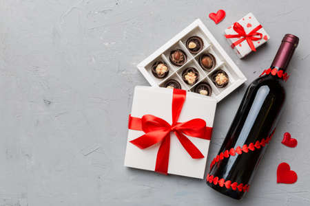 Bottle of red wine on colored background for Valentine Day with gift and chocolate. Heart shaped with gift box of chocolates top view with copy space.の写真素材
