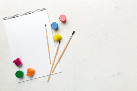Album pages and paints, pencils, brush on a colored background. Top view with empty space. workplace for creativity. home teaching concept drawing.の写真素材
