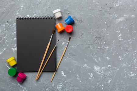 Album pages and paints, pencils, brush on a colored background. Top view with empty space. workplace for creativity. home teaching concept drawing.の写真素材