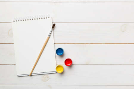Album pages and paints, pencils, brush on a colored background. Top view with empty space. workplace for creativity. home teaching concept drawing.の写真素材