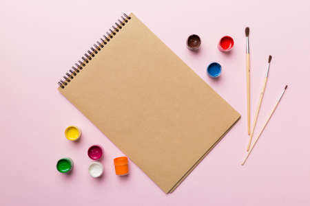 Album pages and paints, pencils, brush on a colored background. Top view with empty space. workplace...
