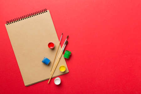 Album pages and paints, pencils, brush on a colored background. Top view with empty space. workplace for creativity. home teaching concept drawing.の写真素材