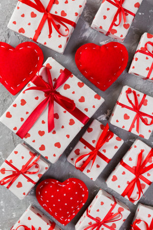 Valentine or other holiday handmade present in paper with red hearts and gifts box in holiday wrapper. Present box of gift on gray cement table top view with copy space, empty space for design.の写真素材