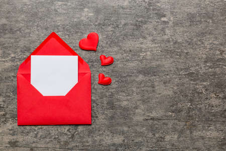 Red paper envelope with empty white card and heart on colored background. top view valentines day...