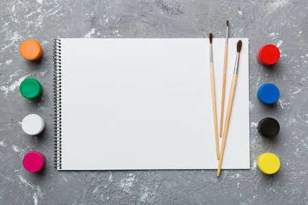 Album pages and paints, pencils, brush on a colored background. Top view with empty space. workplace for creativity. home teaching concept drawing.の写真素材