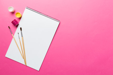 Album pages and paints, pencils, brush on a colored background. Top view with empty space. workplace for creativity. home teaching concept drawing.の写真素材