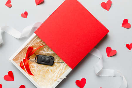 Black car key in a present box with a ribbon and red heart on colored background. Valentine day...
