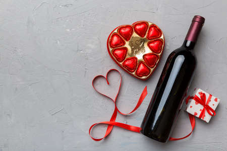 Bottle of red wine on colored background for Valentine Day with gift and chocolate. Heart shaped with gift box of chocolates top view with copy space.の写真素材