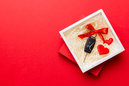 Black car key in a present box with a ribbon and red heart on colored background. Valentine day...