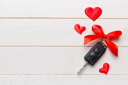 Car key with a red bow and a heart on Colored table. Giving present or gift for valentine day or christmas, Top view with copy space.の写真素材