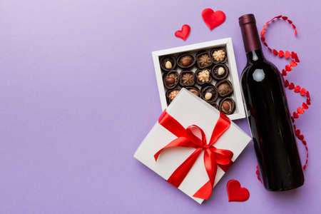 Bottle of red wine on colored background for Valentine Day with gift and chocolate. Heart shaped...