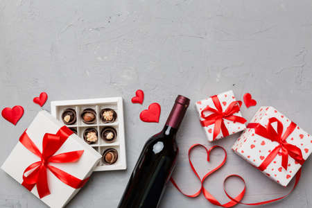 Bottle of red wine on colored background for Valentine Day with gift and chocolate. Heart shaped with gift box of chocolates top view with copy space.の写真素材