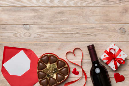 Bottle of red wine on colored background for Valentine Day with gift box, envelope and chocolate. Heart shaped with gift box of chocolates top view with copy space.の写真素材