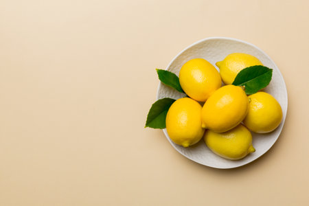 Fresh cutted lemon and whole lemons over round plate on colored background. Food and drink...