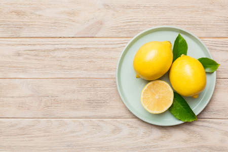 Fresh cutted lemon and whole lemons over round plate on colored background. Food and drink ingredients preparing. healthy eating theme top view with copy space.の写真素材