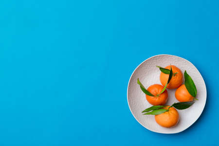 Fresh cutted clementines and whole mandarin over round plate on colored background. Food and drink...