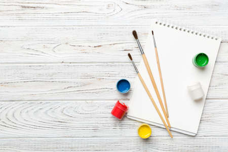 Album pages and paints, pencils, brush on a colored background. Top view with empty space. workplace for creativity. home teaching concept drawing.の写真素材