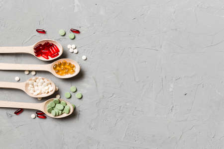 Top view Variety of vitamin and mineral pills in wooden spoon on Colored background. Top view of...