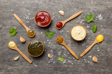 Different sauces in spoons on table background, flat lay top view.