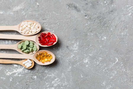 Top view Variety of vitamin and mineral pills in wooden spoon on Colored background. Top view of...